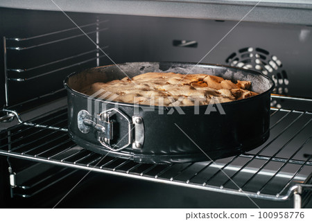 Baking dish with apple pie stands in black oven. Homemade seasonal bakery Baking dish with apple pie stands in black oven. Homemade seasonal bakery 100958776