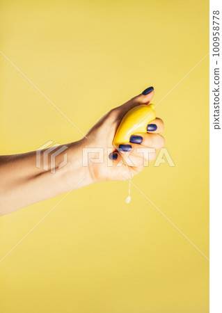 Female hand with blue nails hold fresh lemon isolated on yellow. Squeeze out juice. Finger crush. Vertical, copy space 100958778
