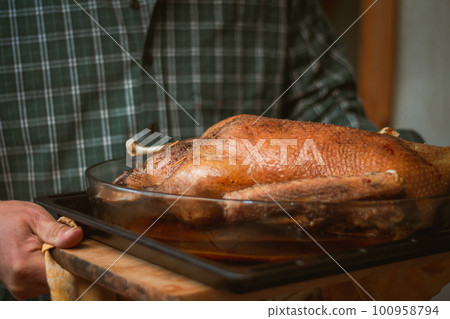 Man in green checkered shirt carries baked goose or turkey on baking sheet 100958794