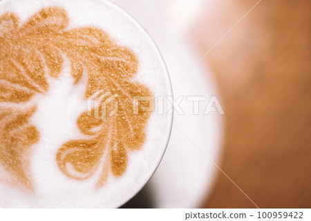 Delicious cappuccino coffee in cup mug glass latte with sour cream milk foam with pattern spike on white ceramic plate 100959422