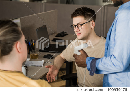 IT Development Team Working on VR Project. Man wearing VR headset, playing and touching something in the virtual world. Diverse men programmers using VR technologies and computer to create video game. 100959476