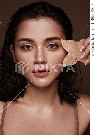 Beautiful young girl with natural nude make-up with gua sha for facial massage in hands. Beauty face. 100959509