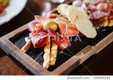 a wooden tray with snacks made of dried meat, sausage, cheese and potato chips. a wooden tray with snacks made of dried meat, sausage, cheese and potato chips. 100960285