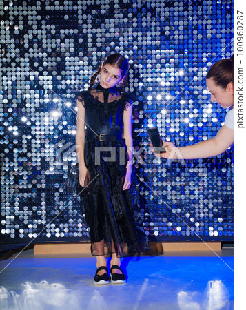 cute teen girl with pigtail in a black long curvy dress at the disco. shiny wall cute teen girl with pigtail in a black long curvy dress at the disco. shiny wall 100960287