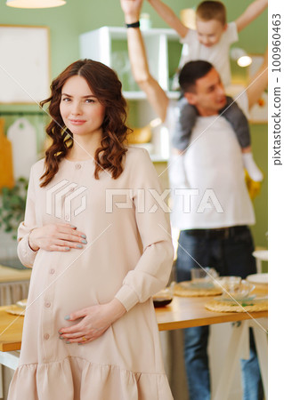 pregnant mom against the background of son and dad In the kitchen. pregnant mom against the background of son and dad In the kitchen. 100960463
