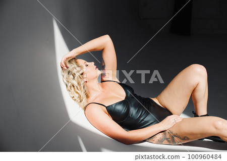 a portrait of a sexy blonde with tattoos in a leather swimsuit and boots. 100960484