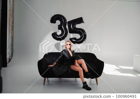 a sexy blonde in a black on the couch. balloons of numbers thirty-five a sexy blonde in a black on the couch. balloons of numbers thirty-five 100960491