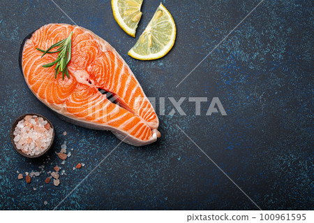 Fresh raw salmon fillet steak with rosemary on dark blue rustic stone background with rose salt and lemon top view, healthy balanced diet and nutrition Fresh raw salmon fillet steak with rosemary on dark blue rustic stone background with rose salt and lemon top view, healthy balanced diet and nutrition 100961595