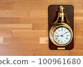 A gold-plated clock with a large bell against a background of wooden floors 100961680