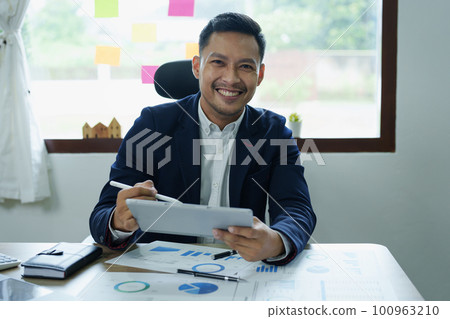 Concept of the impact of warring countries, male economists are using tablets to consult with marketing staff or accountants to adjust production and investment strategies to the current situation 100963210