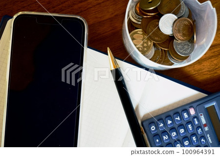 Blank notebook, smartphone, calculator, pen, various coins Blank notebook, smartphone, calculator, pen, various coins 100964391