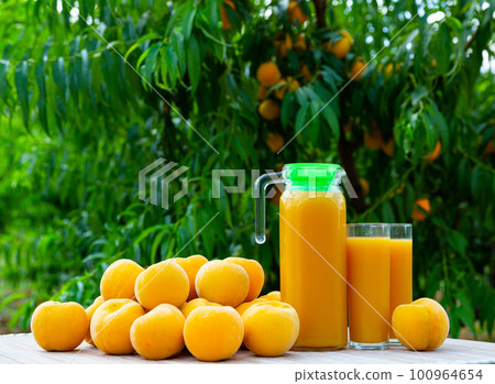Fresh yellow peaches and juice under green tree Fresh yellow peaches and juice under green tree 100964654