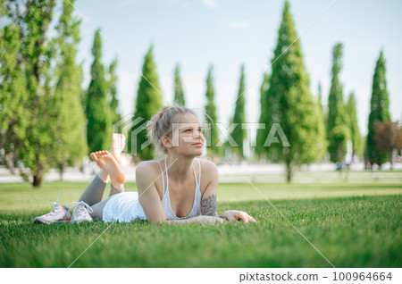 Attractive sportive girl lies on the grass and relaxes in park Attractive sportive girl lies on the grass and relaxes in park 100964664