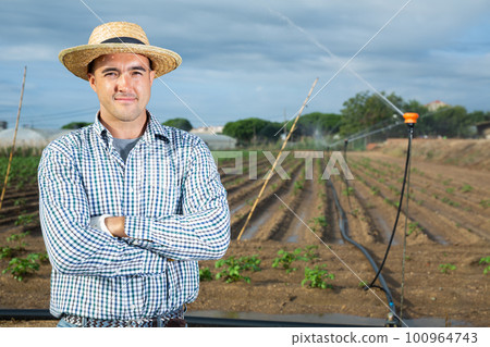 Horticulturist standing in farm field with irrigation system Horticulturist standing in farm field with irrigation system 100964743