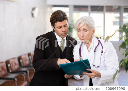 Adult man in suit and elderly woman doctor with folder of documents 100965098