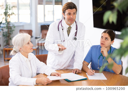 Group of professional doctors sitting at table and discussing diagnosis and treatment of patients during medical council Group of professional doctors sitting at table and discussing diagnosis and treatment of patients during medical council 100965200