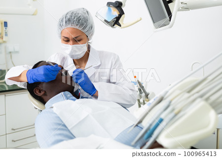Orthodontist using tools and curing toothache of african-american man 100965413