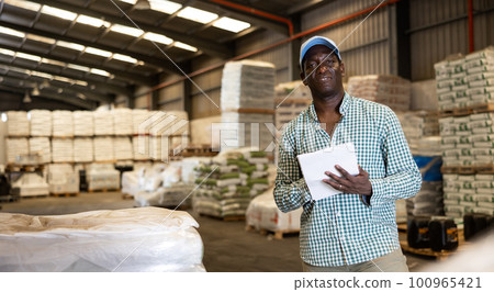 African american man manager leads the accounting of materials in large warehouse 100965421