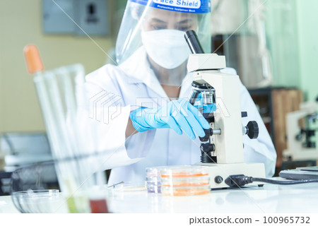 Woman scientist hand write note information in medical lab look at science microscope medical test, research biology chemistry. Asian Females technician laboratory analyzing blood test pharmaceutical Woman scientist hand write note information in medical lab look at science microscope medical test, research biology chemistry. Asian Females technician laboratory analyzing blood test pharmaceutical 100965732