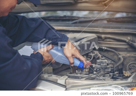 Car Mechanic man hands pouring Deionized purified Distilled water for car battery mechanical service. Close up hands man hold Deionized Distilled liquid water bottle at garage auto mobile car service 100965769