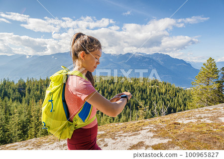 Running trail runner looking sport and fitness smartwatch for training data. Runner woman running cross-country trail run training hiking outside in mountains. Squamish, British Columbia Canada 100965827