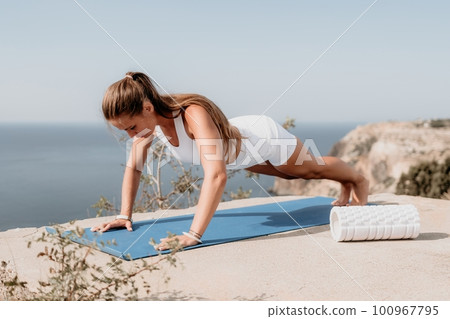Fitness woman sea. Outdoor workout on yoga mat roller in park near to ocean beach. Female fitness pilates yoga routine concept. Healthy lifestyle. Happy fit woman exercising with rubber band in park. Fitness woman sea. Outdoor workout on yoga mat roller in park near to ocean beach. Female fitness pilates yoga routine concept. Healthy lifestyle. Happy fit woman exercising with rubber band in park. 100967795