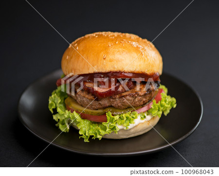 Big tasty burger with beef patty, lettuce, bacon and pickle on black background Big tasty burger with beef patty, lettuce, bacon and pickle on black background 100968043