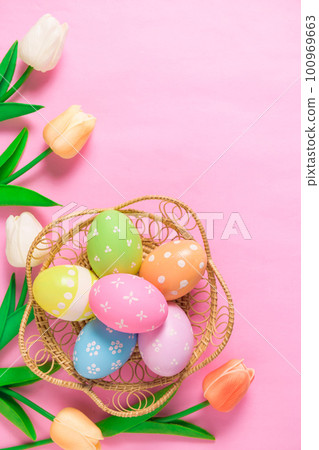 Happy Easter holiday greeting card concept. Colorful Easter Eggs and spring flowers on pastel pink background. Flat lay, top view, copy space. 100969663