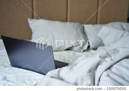 Opened laptop in unmade bed with pillows and crumpled bedsheets at morning. Comfortable workplace for freelancer, work from home Opened laptop in unmade bed with pillows and crumpled bedsheets at morning. Comfortable workplace for freelancer, work from home 100970008