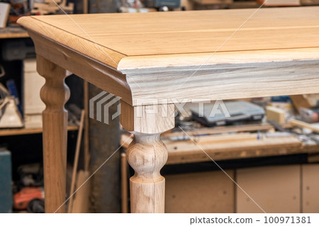 Wooden dining table with carved leg of solid oak and metal frame build process in workshop close up view 100971381