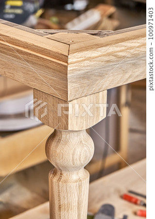 Wooden dining table with carved leg of solid oak and metal frame build process in workshop close up view Wooden dining table with carved leg of solid oak and metal frame build process in workshop close up view 100971403