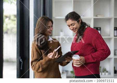 Two diverse female smiling while working together at a boardroom table during a meeting in a modern office Two diverse female smiling while working together at a boardroom table during a meeting in a modern office 100971511