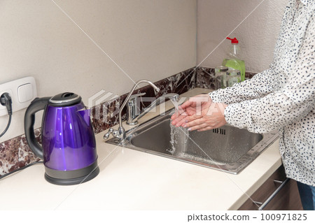 A woman washes her hands under tap water. Hand disinfection, hygiene 100971825