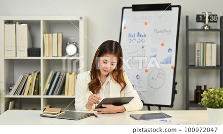 Focused female manager using digital tablet working on financial and marketing projects in modern office 100972047