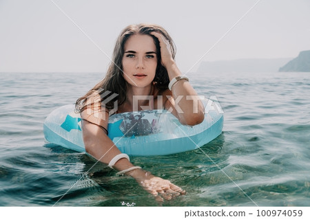Woman summer sea. Happy woman swimming with inflatable donut on the beach in summer sunny day, surrounded by volcanic mountains. Summer vacation concept. Woman summer sea. Happy woman swimming with inflatable donut on the beach in summer sunny day, surrounded by volcanic mountains. Summer vacation concept. 100974059