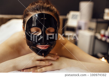 Pretty brunette female with cosmetic mask on her face. Skin care c 100974382