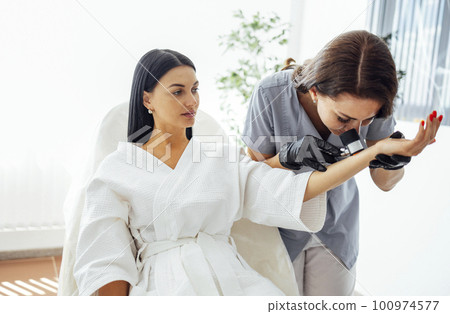Doctor dermatologist examines skin of client face of beauty salon with a dermatological lens Doctor dermatologist examines skin of client face of beauty salon with a dermatological lens 100974577