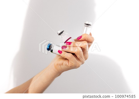 Close up of female hand holds bottles with cosmetic preparations and serums Close up of female hand holds bottles with cosmetic preparations and serums 100974585