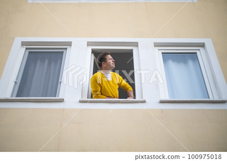 caucasian guy looking from the widnow spying on his neighbours 100975018