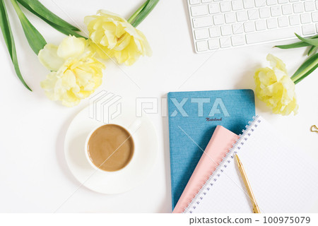 Modern white office desk table with a cup of coffee, computer keyboard, notebooks, pen, flowers and other accessories. Top view with a space to copy on a white background. Top view, flat lay. 100975079