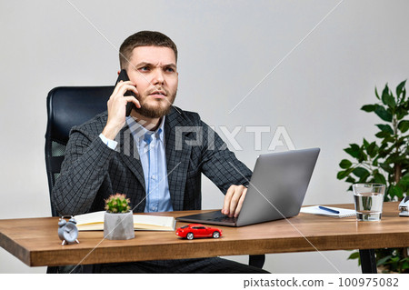 businessman sitting on chair at desk and talking on the phone businessman sitting on chair at desk and talking on the phone 100975082