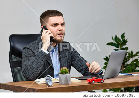 businessman sitting on chair at desk and talking on the phone 100975083