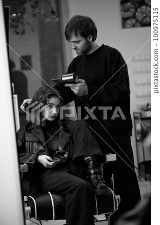 man hairdresser dries female hair with hairdryer after washing 100975115