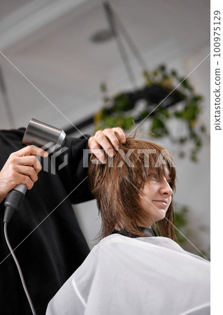 man hairdresser dries female hair with hairdryer after washing 100975129