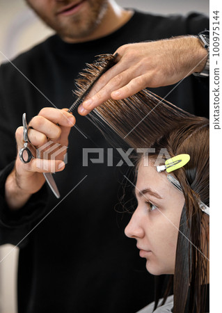 Professional male hairdresser cutting female hair in salon 100975144
