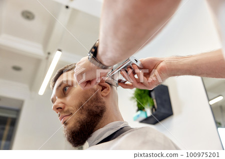 Barber trim hair with clipper on handsome bearded man Barber trim hair with clipper on handsome bearded man 100975201