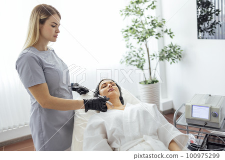 Beautiful caucasian young woman is doing a mole removal procedure in a modern beauty cosmetic dermatological clinic 100975299