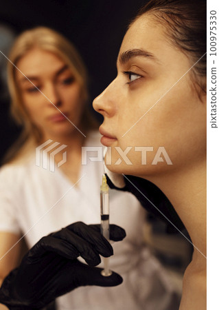 Female cosmetologist in transparent gloves makes an injection in the lower jaw of her client Female cosmetologist in transparent gloves makes an injection in the lower jaw of her client 100975330