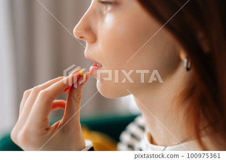 Close-up face of ill young woman taking pill. Closeup side view of sick redhead female holding medicament at mouth. Close up of depressed lady handing antidepressants tablet meds to mouth. Close-up face of ill young woman taking pill. Closeup side view of sick redhead female holding medicament at mouth. Close up of depressed lady handing antidepressants tablet meds to mouth. 100975361