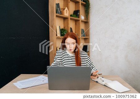 Portrait of positive female freelancer with broken right hand wrapped in white gypsum bandage having online video call, working remotely on laptop computer sitting at table in home office room. Portrait of positive female freelancer with broken right hand wrapped in white gypsum bandage having online video call, working remotely on laptop computer sitting at table in home office room. 100975362